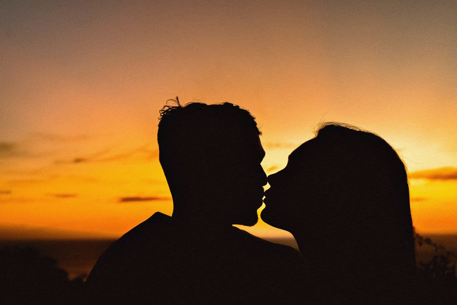 Silhouette of a couple sharing a kiss with a vibrant sunset in the background, evoking romance and warmth.